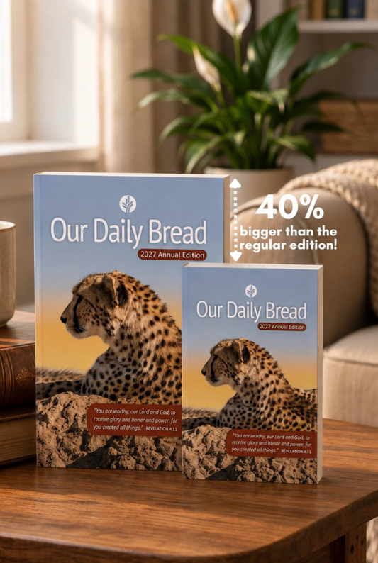Two boxed copies of 'Our Daily Bread 2027 Annual Edition' displayed on a wooden table in a cozy living room setting,  A promotional arrow overlay notes '40% bigger than the regular edition!'.